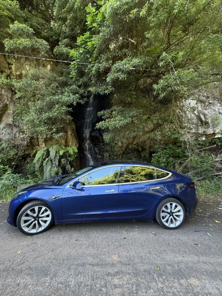 Tesla Model 3 rental car parked next to a waterfall in Madeira